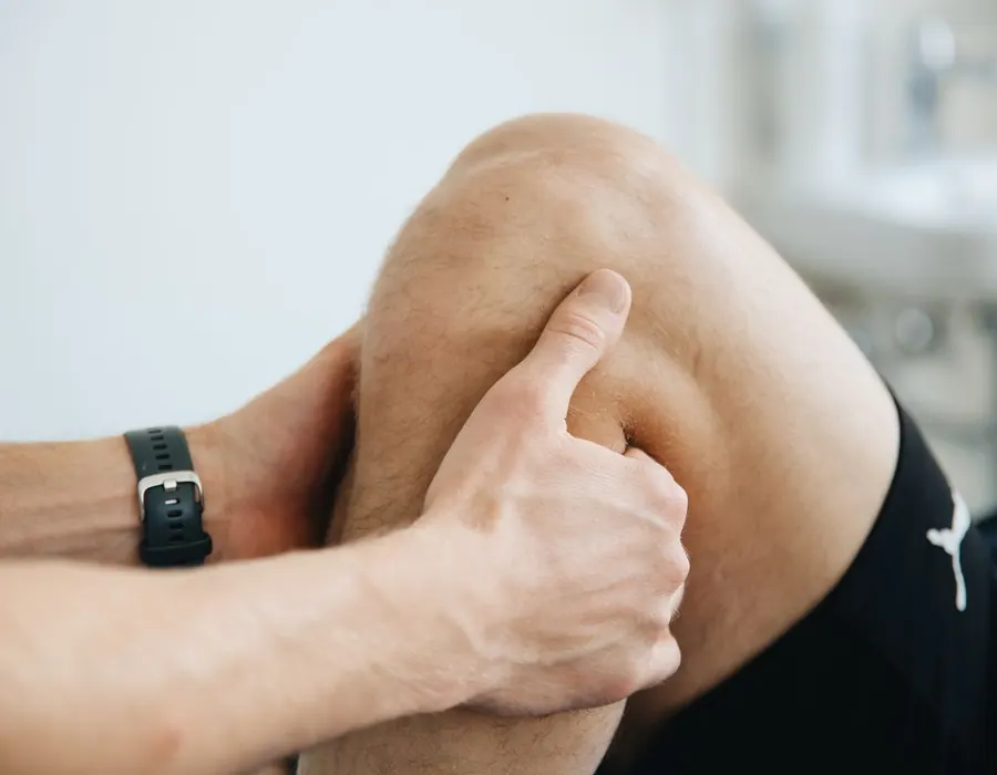 Hierojan peukalo painaa polvitaipeen lihasta; asiakkaalla on urheilushortsit ja hierojan ranteessa urheilukello.