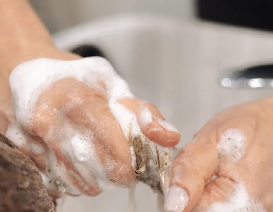 Kädet hierovat shampoovaahtoa hiuksiin pesualtaan ääressä