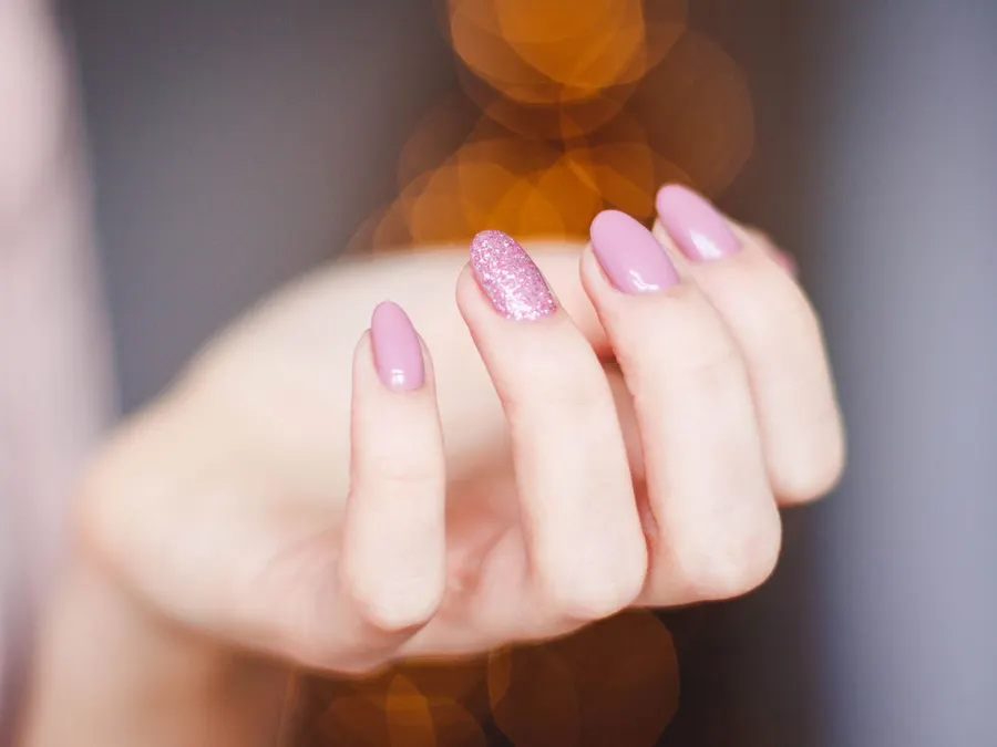 Käsi, jonka kynnet on lakattu vaaleanpunaisiksi ja yksi kynsi glitterillä